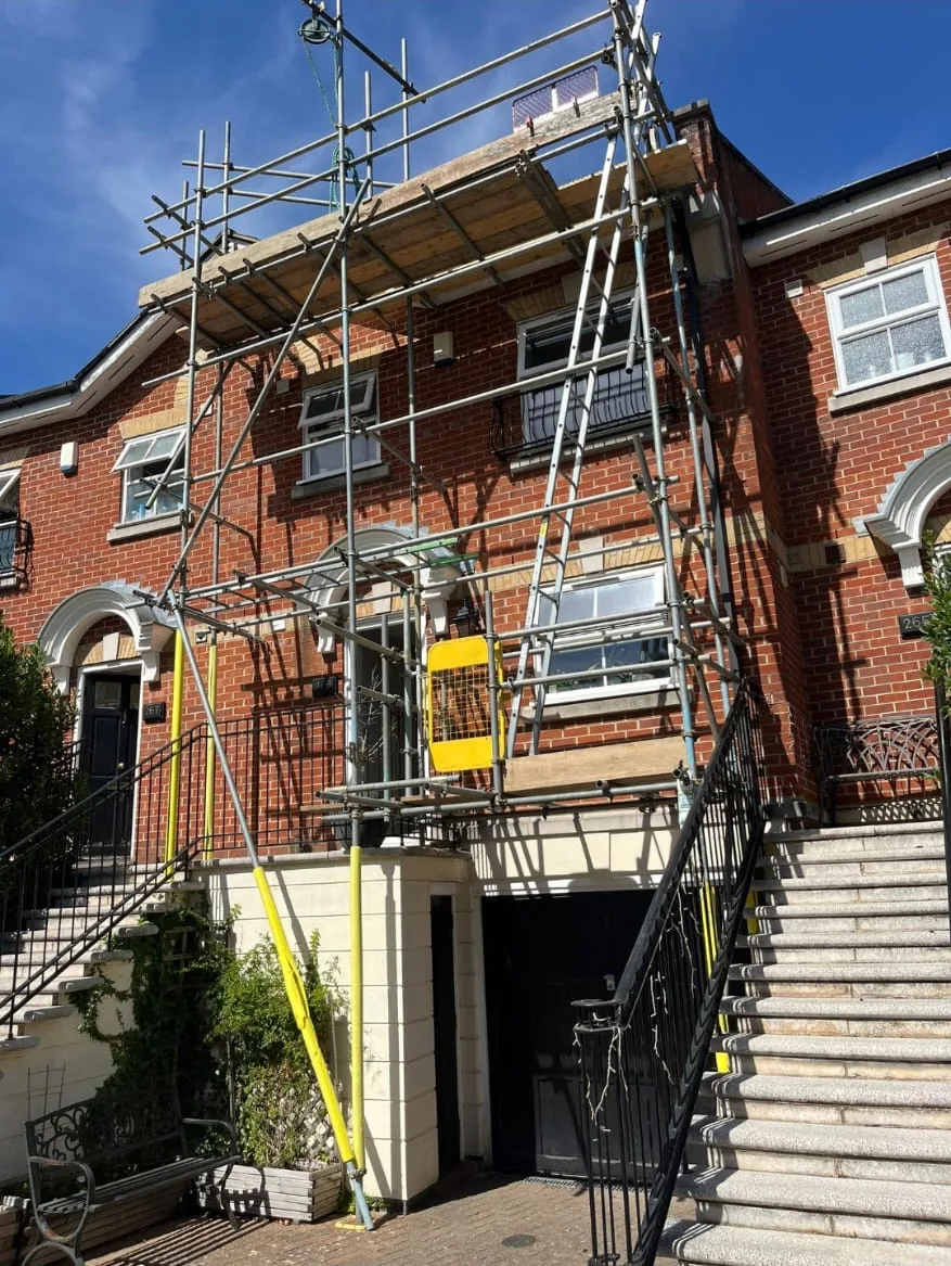 Roof access scaffold across a red brick house above basement steps