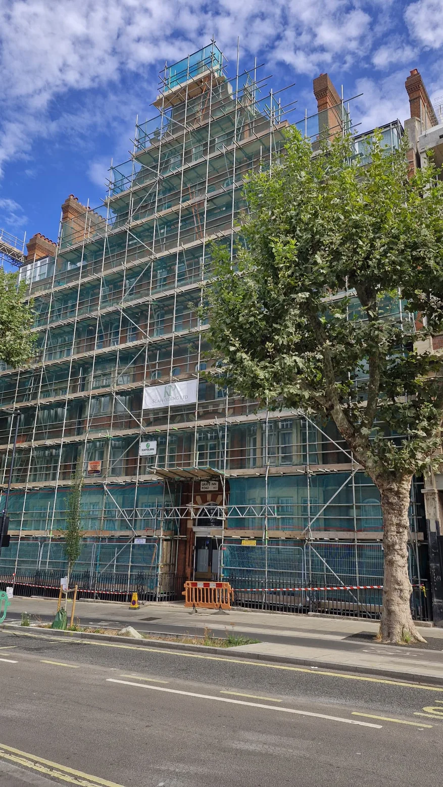 Angled view of full building scaffolding and protective netting beside a Central London street
